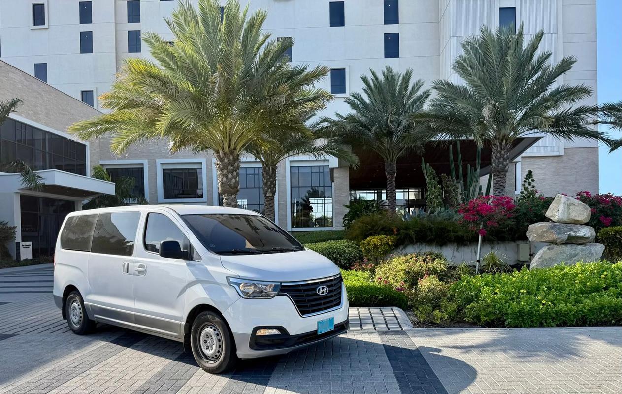 White Hyundai H-1 SupAce Transfers private transfer van parked at the St. Regis Aruba resort entrance in Palm Beach on a sunny day